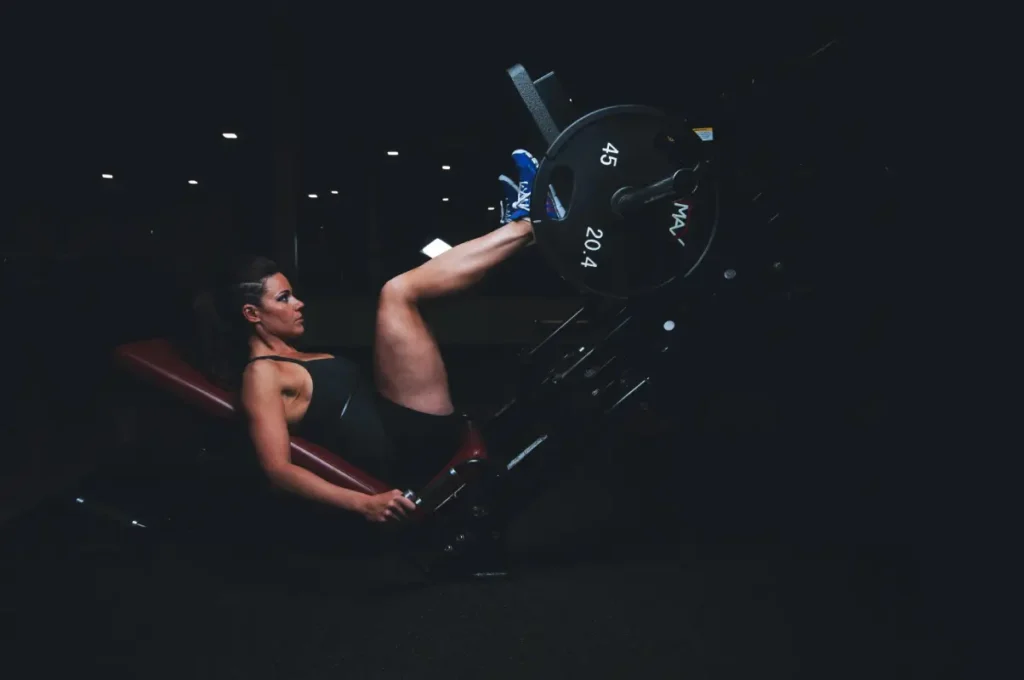 Woman performing a leg press exercise on a leg press machine in a gym setting, focusing on lower body strength.