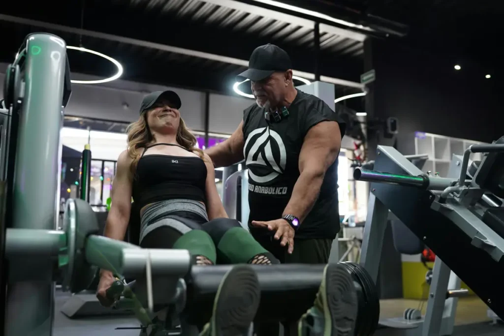 Woman performing leg extensions on a machine under the supervision of a personal trainer
