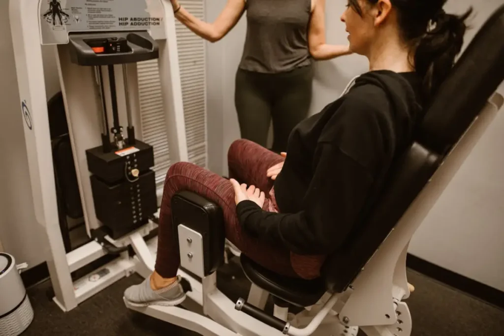 Woman performing inner thigh workout using an adductor machine under guidance